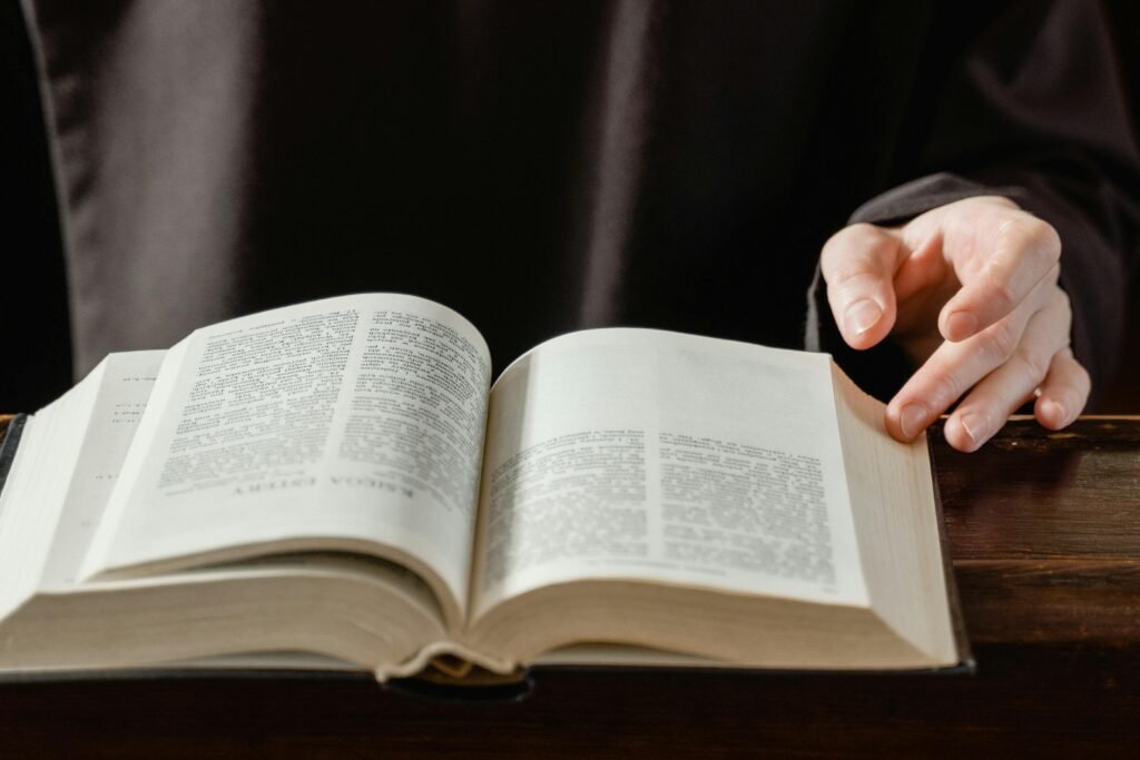 Close-up of a person turning pages of an open Bible on a wooden desk.